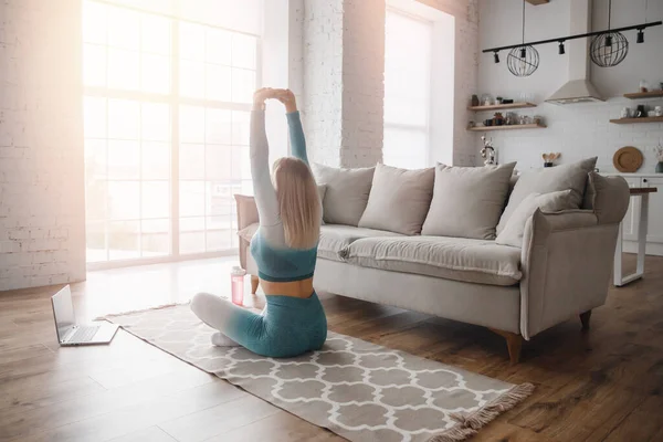 İnternette yoga yapan bir kadın dizüstü bilgisayarla video izliyor. Evde konsept fitness çalışması — Stok fotoğraf