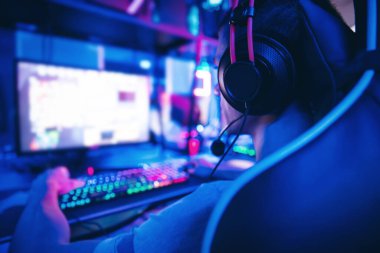 Genç oyuncu internet kulübü kafesinde kulaklıkla video oyunu oynuyor, mavi renkte. Esports konsepti