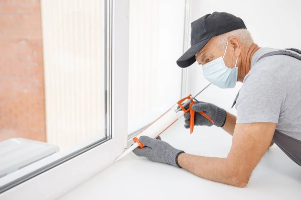 Trabalhador em máscara médica use pistola de tubo de silicone para reparar e instalar a janela — Fotografia de Stock