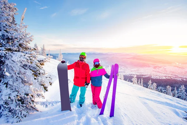 Szerető pár snowboard és síelő kéz a kézben a háttérben a hegyek a téli erdőben, Napfény. Koncepcionális síközpont — Stock Fotó