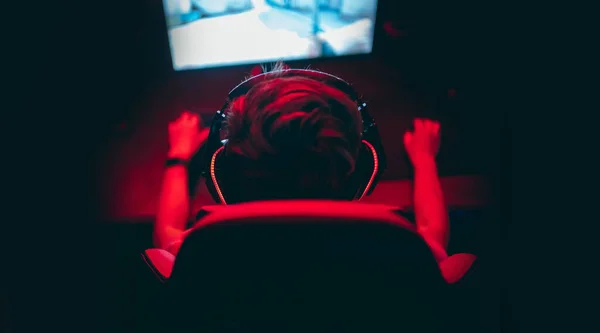 Jugador profesional jugando torneos de juegos en línea ordenador PC con auriculares, fondo rojo y azul borrosa —  Fotos de Stock