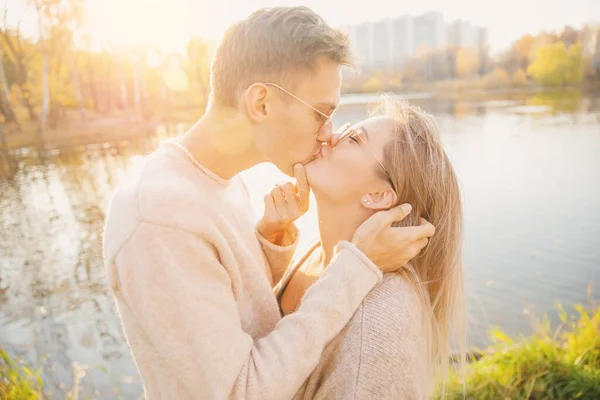 Amante casal em óculos de sol forma redonda abraçar suéter e beijo contra o pano de fundo do parque de outono — Fotografia de Stock