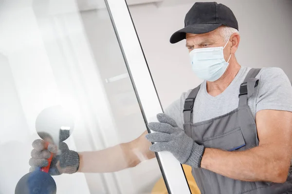 Trabalhador homem em máscara médica instala plástico upvc janelas e portas brancas com elevador a vácuo — Fotografia de Stock