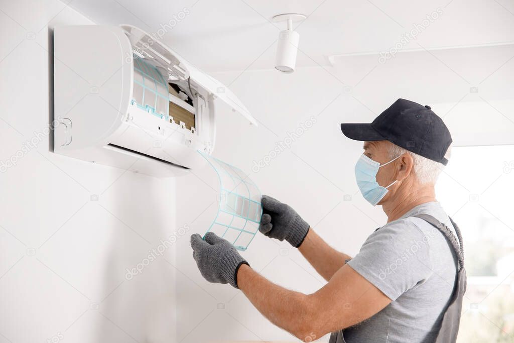 Air conditioner cleaning. Worker in gloves and medical mask checks filter