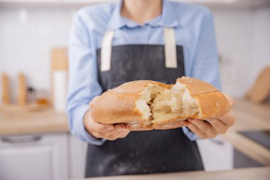 Fırıncı elleri taze, yuvarlak buğday ekmeğini iki parçaya böler.