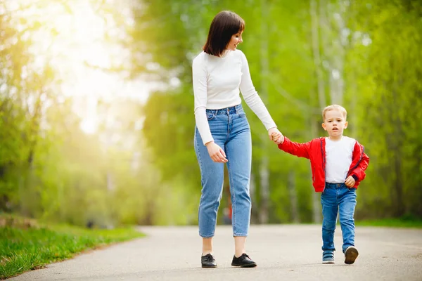 Feliz família caucasiana mãe e filho criança estão andando no parque de mãos dadas, luz solar — Fotografia de Stock