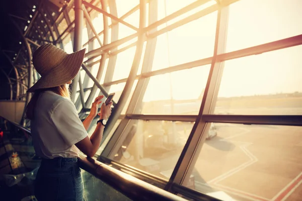 Flygplats, kvinna väntar på plan i terminal på bakgrundsfönster, skriver meddelanden till vänner och släktingar i budbärare — Stockfoto