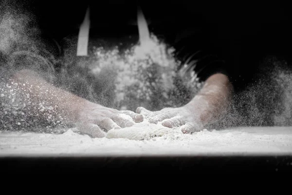 Hands of male baker preparing yeast dough with white flour dust on black background, scoop out for pasta and pizza