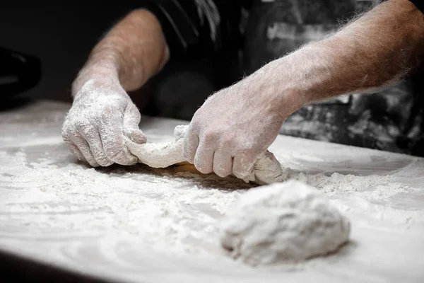 Harina blanca vuela en el aire sobre fondo negro, pastelero aplaude las manos y prepara la masa de levadura para la pasta de pizza — Foto de Stock