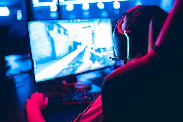 Joueur professionnel jouant tournois de jeux en ligne PC ordinateur avec écouteurs, fond rouge et bleu flou — Photo