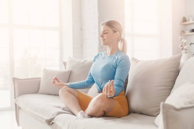 Güzel beyaz kadın yoga nilüfer pozisyonunda oturmuş meditasyon yapıyor. Kanepe oturma odasında rahatlamak kavramı