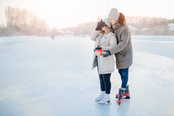 冬天，男人用手合上眼睛的女孩，并在冰球场上放上蝴蝶结礼品盒，这是情人节的概念 — 图库照片