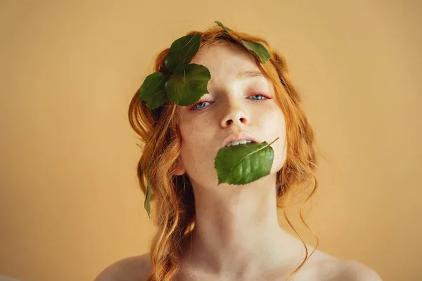 Hermosa joven pelirroja ojos azules con hojas verdes en la cara. Naturaleza cosmética orgánica y maquillaje —  Fotos de Stock