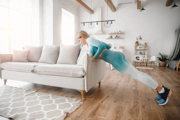 Sıska, sportif bir kadın evdeki mutfakta kanepeyle karın kası egzersizi yapıyor. — Stok fotoğraf