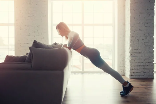 Menina atlética esportiva magro faz exercícios push-up com objetos de sofá improvisados em casa. Conceito Desportos de estilo de vida para pandemia — Fotografia de Stock