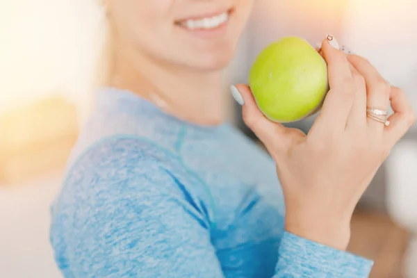 Νέα και ευτυχισμένη γυναίκα τρώει υγιεινό μήλο με πράσινα φρέσκα συστατικά στην κουζίνα — Φωτογραφία Αρχείου