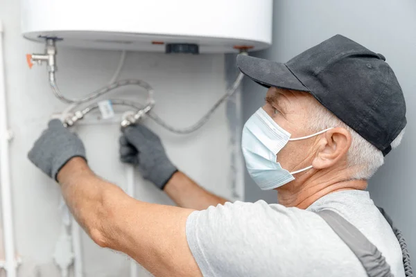 Encanador homem em máscara médica instalar caldeira aquecedor de água no banheiro — Fotografia de Stock