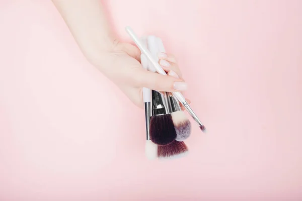Chica artista mano con pinceles maquillaje sobre fondo de color rosa. Vista superior plano laico — Foto de Stock