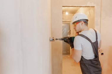 Pnömatik çekiç delici ve elmas kaplama delgisi olan tamirci elektrik kablosu, soket, anahtar için duvarda delik açıyor.