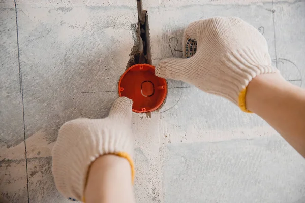 Trabalhador construtor instala caixa de plástico sob tomada elétrica na parede do furo — Fotografia de Stock