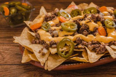 Nacho cips Mısır kıyma, eritilmiş peynir, jalapenos ile süslenmiş içinde plaka üzerinde ahşap masa Meksika baharatlı gıda Meksika biber