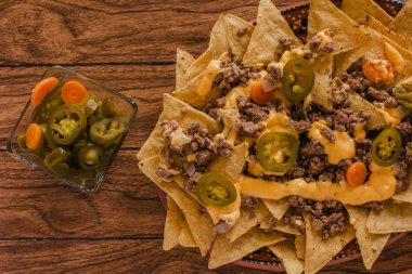 Nacho cips Mısır kıyma, eritilmiş peynir, jalapenos ile süslenmiş içinde plaka üzerinde ahşap masa Meksika baharatlı gıda Meksika biber