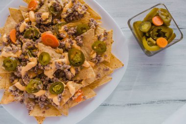 Nacho cips Mısır kıyma, eritilmiş peynir, jalapenos ile süslenmiş içinde plaka üzerinde ahşap masa Meksika baharatlı gıda Meksika biber