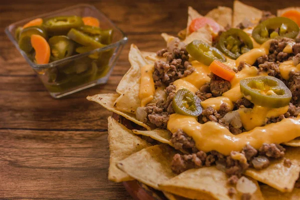 nacho chips corn garnished with ground beef, melted cheese, jalapenos peppers in plate on wooden table mexican spicy food in mexico