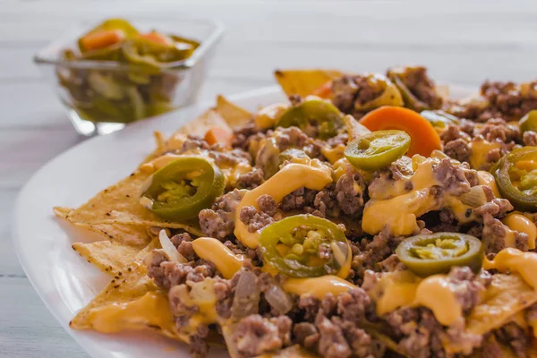 Nacho cips Mısır kıyma, eritilmiş peynir, jalapenos ile süslenmiş içinde plaka üzerinde ahşap masa Meksika baharatlı gıda Meksika biber