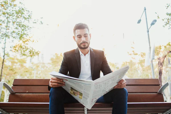 young man reading newspaper on a bench