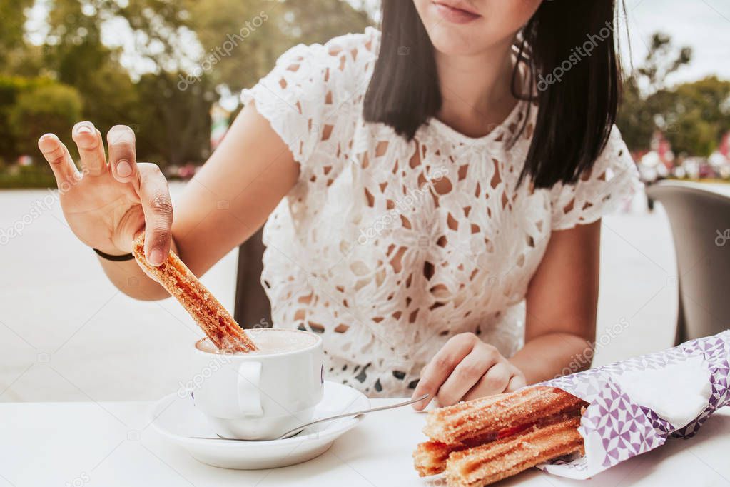 Mexican girl eating traditional Churros, a fried pastry with chocolate in coffee shop in Mexico, Hispanic female