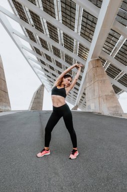 Latin Amerika 'nın kentsel bölgesinde spor kıyafetleri içinde esneyen ve egzersiz yapan genç İspanyol kadın.