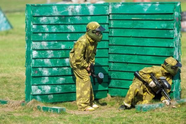 彩弹球员在伪装制服和防护面具与枪在球场上 在夏季拍摄的敌人 — 图库照片