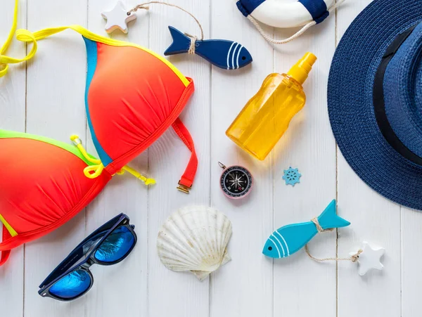 Yaz aksesuarları kadın için: hasır şapka, pusula, kabuklar, Mayo, Gözlük, güneş sprey, ahşap arka plan üzerinde balıklar. Seyahat, yaz satış konsepti
