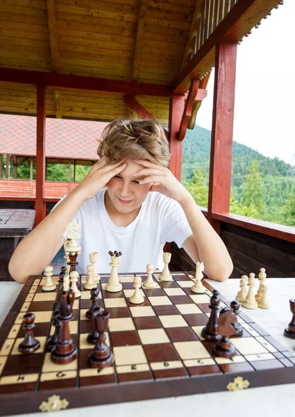 年轻的男孩正在考虑在棋盘上的移动 教育理念 象棋课 智力游戏 — 图库照片