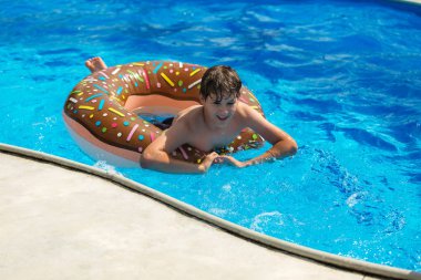 sportif yakışıklı çörek yüzüklü havuzunda yüzüyor ve eğlenir, gülümsüyor. Çocuklar, özel günler, etkin hafta sonları kavramı ile tatil