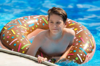 sportif yakışıklı çörek yüzüklü havuzunda yüzüyor ve eğlenir, gülümsüyor. Çocuklar, özel günler, etkin hafta sonları kavramı ile tatil