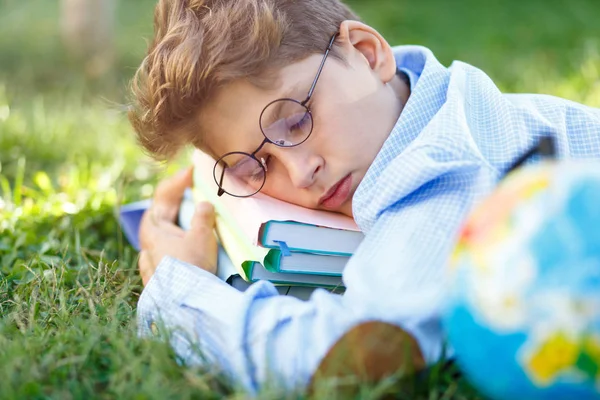 かわいい少年が青いシャツを着て丸メガネは 彼は本公園の芝生の上に寝ています 教育学校コンセプトに戻る — ストック写真