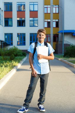 Sevimli, güzel, Genç 11 yaşında mavi gömlekli çocuk kitaplarıyla onun okulun önünde duruyor. Eğitim, okul kavramı başa