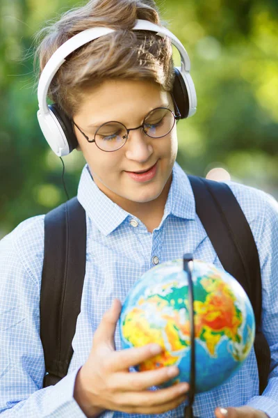 cute, young boy in blue shirt holds a globe and workbooks in his arms in the park in the summer. Back to school, education concept