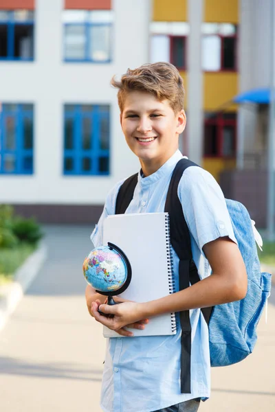 可爱的小男孩穿着蓝色衬衫 背包和工作簿在他的学校前面握着地球仪 回到学校概念 — 图库照片