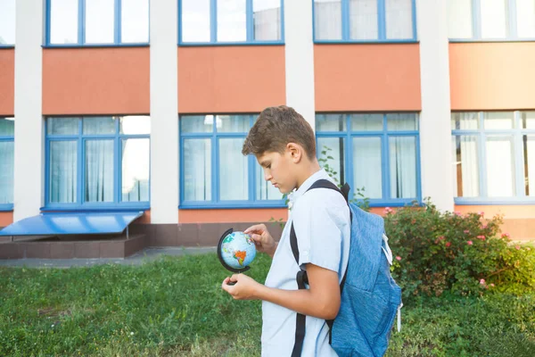 可爱的小男孩穿着蓝色衬衫 背包和工作簿在他的学校前面握着地球仪 回到学校概念 — 图库照片
