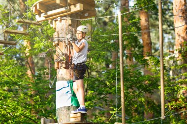 şirin, sportif çocuk kask ve güvenlik ekipmanları ile macera ip etkinlik parkta Beyaz tişörtlü. Genç çocuk oynamaya ve sahip eğlenceli aktiviteler açık havada yaptığını. Hobi, aktif yaşam tarzı kavramı