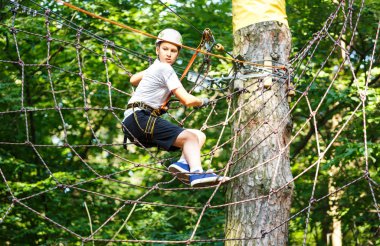 şirin, sportif çocuk kask ve güvenlik ekipmanları ile macera ip etkinlik parkta Beyaz tişörtlü. Genç çocuk oynamaya ve sahip eğlenceli aktiviteler açık havada yaptığını. Hobi, aktif yaşam tarzı kavramı