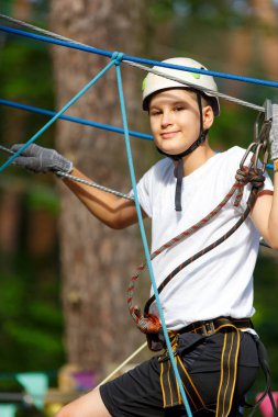 şirin, sportif çocuk kask ve güvenlik ekipmanları ile macera ip etkinlik parkta Beyaz tişörtlü. Genç çocuk oynamaya ve sahip eğlenceli aktiviteler açık havada yaptığını. Hobi, aktif yaşam tarzı kavramı