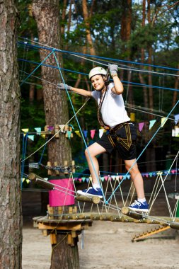şirin, sportif çocuk kask ve güvenlik ekipmanları ile macera ip etkinlik parkta Beyaz tişörtlü. Genç çocuk oynamaya ve sahip eğlenceli aktiviteler açık havada yaptığını. Hobi, aktif yaşam tarzı kavramı
