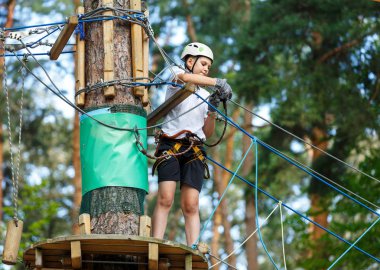 şirin, sportif çocuk kask ve güvenlik ekipmanları ile macera ip etkinlik parkta Beyaz tişörtlü. Genç çocuk oynamaya ve sahip eğlenceli aktiviteler açık havada yaptığını. Hobi, aktif yaşam tarzı kavramı
