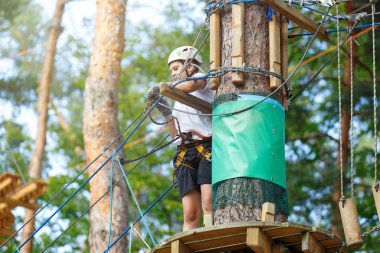 şirin, sportif çocuk kask ve güvenlik ekipmanları ile macera ip etkinlik parkta Beyaz tişörtlü. Genç çocuk oynamaya ve sahip eğlenceli aktiviteler açık havada yaptığını. Hobi, aktif yaşam tarzı kavramı