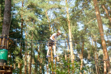 şirin, sportif çocuk kask ve güvenlik ekipmanları ile macera ip etkinlik parkta Beyaz tişörtlü. Genç çocuk oynamaya ve sahip eğlenceli aktiviteler açık havada yaptığını. Hobi, aktif yaşam tarzı kavramı