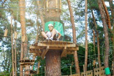 şirin, sportif çocuk kask ve güvenlik ekipmanları ile macera ip etkinlik parkta Beyaz tişörtlü. Genç çocuk oynamaya ve sahip eğlenceli aktiviteler açık havada yaptığını. Hobi, aktif yaşam tarzı kavramı
